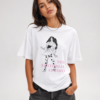 Mannequin femme portant un t-shirt oversize blanc imprimé avec l'illustration 'Mona Lisa Polka Dotted Girl' et le logo rose 'THE EDITORIAL STUDIO'. Tenue avec pantalon large noir et sac à main.